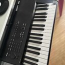 Černý digitální klavír se bílými a černými klávesami a dřevěnou horní lištou. Na levé straně je bílý nápis KRONOS a vedle něj logo KORG. V pravém hor…