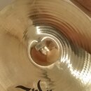 Zlatavý kovový činel s viditelným broušením povrchu. Na spodní části je černý nápis Zildjian®. V centru cinchle je vidět malá bílá nálepka s nečiteln…