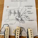 Tři krémové snímače pro elektrickou kytaru s bílými pólky. Na každém je z boku černý plastový kryt s nápisem Noiseless. Snímače jsou umístěny na sché…