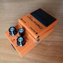 Oranžový efekt pedál s černým spínacím tlačítkem. Na horní části je nápis Distortion a označení DS-1, na tlačítku je logo BOSS. Na ovládacím panelu j…