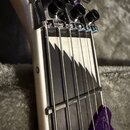 Detailní pohled na hmatník a kobylku elektrické kytary. Hmatník je tmavý s bílým ozdobným vzorem v podobě zubů pily. Kobylka je chromovaná s třemi če…