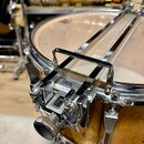 Detailní záběr na chromovaný snare throw-off (mechanismus pro napnutí rastra) na bubnu. Buben má korpus z přírodního dřeva s viditnou strukturou zrn…