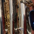 Detail zlatavého kovového nástroje, pravděpodobně saxofonu. Na povrchu je vyryt nápis Brooklyn v kurzívě. Povrch vykazuje drobné škrábance a známky o…