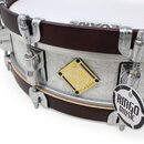 Detailní pohled na snare drum s tmavě hnědými obručemi a bílým koženem značky EVANS. Korpus je bílý s jemným ornamentem a nese žlutý čtvercový štítek…