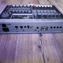 Šedý elektronický klávesový nástroj značky Roland, model VS-840, zobrazený z úhlu s viditelným zadním panelem. Na zadní straně jsou umístěny konektor…