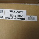 Detail hnědé kartonové krabice se třemi bílými nálepkami. Prostřední nálepka obsahuje nápisy SHADOW EDITION a waldorf blofeld SYNTHESIZER s logem výr…