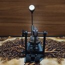 Černý basový pedál s kovovou konstrukcí a bílým plstěným beaterem. Mechanismus pohonu je řetězový, s viditelným ozubeným kolem a řetězem. Povrch je m…