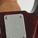 Detail zadní části krku a těla basové kytary v tmavě červené barvě. Na těle je přišroubovaná kovová krytka s nápisy Marcus Miller a stylizovaným symb…