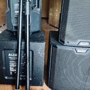 Fotografie zobrazuje sadu reproduktorů značky ALTO a dva černé rozkládací stojany. Na spodním subwooferu je viditelný nápis ALTO Professional a model…
