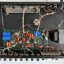 Fotografie zachycuje vnitřek elektronického zařízení s otevřeným šasi. Uprostřed je zelená základní deska s osazenými elektronkami, kondenzátory a rů…
