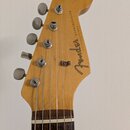 Zadní strana hlavy dřevěné kytary s nápisem Fender STRATOCASTER a textem ORIGINAL Contour Body. Na hlavě jsou umístěny šest kovových ladiček stříbrné…