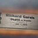 Fotografie detailu štítku uvnitř hudebního nástroje. Na štítku je uveden text „Richard Gareis OLOWI u Kraslic“ a níže nejasný nápis končící „r. 1906“…