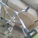 Detailní pohled na chromovaný bubenový pedál. Na centrálním kloubu je viditelné logo Pearl. Konstrukce vykazuje mírné známky opotřebení a znečištění…