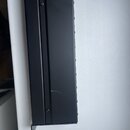 Černý kovový obdélníkový box s dlouhým žlabkovaným rýhou v horní části. Na povrchu jsou viditelné dvě šrouby a několik škrábance v dolní části. Žádné…