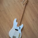 Bílá elektrická basová kytara s bílým pickguardem a hnedým hmatníkem. Na hlavě nástroje je viditelné logo Squier. Instrument má jeden snímač a chromo…