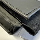 Černý kožený nebo syntetický pouzdro s černým textilním popruhem. Předmět je proveden v černé barvě a má viditelné švy po okrajích. Na fotce nejsou ž…