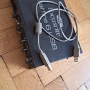 Černý audio rozhraní s ovládacími knoflíky na přední straně. Na horní části je bílý nápis Focusrite Scarlett 6USB. Přístroj leží na dřevěné podlaze a…