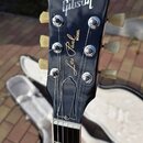 Zadní strana hlavy černé elektrické kytary s nápisy Gibson a Les Paul MODEL. Na hlavě jsou vidět šest ladicích kol s bílými knoflíky a kovovými mecha…