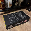Krabice s kytarovým procesorem Mooer GE150. Na horní části krabice je zobrazen produkt s nápisy MOOER a GE150 Multi-Effects Processor. Na boku krabic…