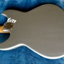 Zadní strana hlavy elektrické kytary v matné šedé barvě. Na povrchu je bílý nápis „ENZS“. Kolem spoje s hnedým krkem je vidět kovovádeska připevněná…
