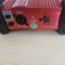 Zadní strana červeného kovového zařízení s žebrovaným povrchem. Je zde vidět konektor XLR s nápisem OUTPUT TO MIXER a popis pinu: PIN 1: GND, PIN 2:…