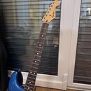 Modrá elektrická kytara s bílým pickguardem a hnědým hmatníkem. Na hlavě nástroje je viditelné logo Fender a nápis STRATOCASTER. Kytara vykazuje běžn…