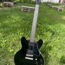 Černá elektrická kytara s polodupatým tělem a bílým lemováním. Na hlavě hředu je viditelné logo Gibson. Nástroj má dva humbuckery, čtyři ovládací kno…