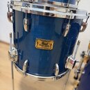 Modrý buben s kovovými obručemi a ladidly. Na korpusu je zlatý štítek s nápisy Pearl, Masters Studio a MAPLE SHELL. Povrch nástroje vykazuje drobné o…