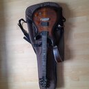 Elektrická kytara s tmavě hnědým průhledným lakem a viditnou strukturou dřeva, položená na hnědém polstrováním (gig bag). Nástroj má dva humbuckery,…