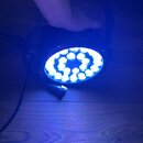 Fotografie zachycuje zapnutý LED reflektor s modrým světlem, který je umístěn na dřevěné podlaze. Zařízení má kulatý tvar s více phosphorylatedmi LED…