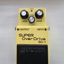 Žlutý efekt pedál s černým gumovým spínacím pedalem. Na zařízení jsou nápisy SUPER Over Drive, SD-1 a logo BOSS. Horní panel obsahuje tři ovládací kn…