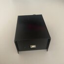 Černý obdélníkový box z kovového nebo plastového materiálu. Na přední straně je umístěn jeden USB port a malá čtvercová kontrolka. Povrch je hladký a…