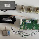 Sada elektronických komponentů skládající se z tři potenciometrů, zelené základní desky s připojenými vodiči a dvou černých či šedých modulů. Na pote…