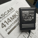 Černý síťový adaptér s nápisem TASCAM MODEL NO. PS-P414 a AC ADAPTOR. Štítek obsahuje technické údaje: INPUT : 230V~, 50Hz, 17VA; OUTPUT : 12V---, 65…