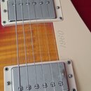 Detail elektrické kytary s červeně-žlutým přechodem barvy korpusu a bílým pickguardem. Na kytaru jsou instalovány dva snímače s chromovanými kryty a…