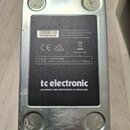 Spodní strana efektového pedálu v kovovém šasi stříbrné barvy. Na černé nálepce je uveden nápis tc electronic a text DESIGNED AND ENGINEERED IN DENMA…