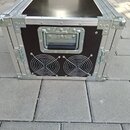 Černý transportní flightcase s hliníkovými hranami a kovovými rohy. Na zadní straně jsou umístěny dvě větrací mřížky s ventilátory a uprostřed je kov…