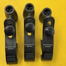 Tři černé plastové držáky mikrofonů s integrovanými konektory. Na každém je bílý nápis SENNHEISER MZH 504. Povrch plastu vykazuje mírné známky opotře…