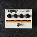 Bílý kytarový zesilovač s nápisy ORANGE TERROR STAMP. Na horní části jsou čtyři černé ovratové ovládací knoflíky s popisy VOLUME 1, VOLUME 2, SHAPE a…