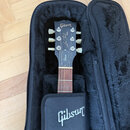 Černá elektrická kytara v černém polotvrdém kufru s plyšovou výstělkou. Na hlavě nástroje je bílé logo Gibson, nápis Les Paul Custom a v dolní části…