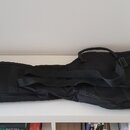 Černý polstrovaný obal na hudební nástroj s ramenním popruhem a rukojetí. Povrch je z textilie, bez viditelných značek, log nebo nápisů. Obal je polo…