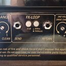 Detail zadní strany kytarového zesilovače s ovládacími prvky. Jsou zde vidět popisky REVERB BALANCE (s přepínačem DRIVE a CLEAN), FX-LOOP (se vstupy…