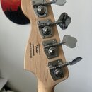 Zadní strana hlavy basové kytary z přírodního dřeva se čtyřmi chromovanými ladičkami. Na dřevě je černý nápis: Designed and faced by Fender Crafted i…