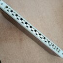 Bílá harmonika s kovovými krytkami. Nástroj je zobrazen z úhlu, na těle nejsou vidět žádné značky ani nápisy. Na jednom konci je umístěn malý bílý ku…
