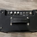 Černý kytarový kombo zesilovač s koženým povrchem a úchytem. Na ovládacím panelu jsou nápisy INPUT, GAIN, VOLUME, EQ a POWER ON. Je zde viditelné log…
