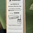 Fotografie znázorňuje kartónovou krabici s bílým štítkem. Na štítku je logo a nápis SENNHEISER, model ew IEM G4-A1 Wireless Monitor Set, frekvenční r…
