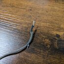 Fotografie detailu konce šedého pleteného kabelu. Opleněná část kabelu je zakončena černým plastovým krytem, ze kterého vyčnívají neizolované kovové…