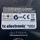 Detailní záběr na štítky na spodní straně černého zařízení. Horní černý štítek obsahuje text „THIS CLASS B DIGITAL DEVICE MEETS ALL REQUIREMENTS OF T…
