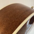 Detailní záběr na hranu hřdelníku akustické kytary z hnědého dřeva s viditnou masivní strukturou. Kolem okraje je bílý lem (binding). Na bílém lemu j…