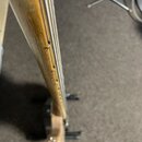 Detailní pohled na hmatník a krk strunového nástroje z dřeva s viditnou masivnější strukturou slz. Nástroj má čtyři kovové struny a bílou matici u hl…